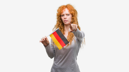 Sticker - Young redhead woman holding flag of Germany pointing with finger to the camera and to you, hand sign, positive and confident gesture from the front