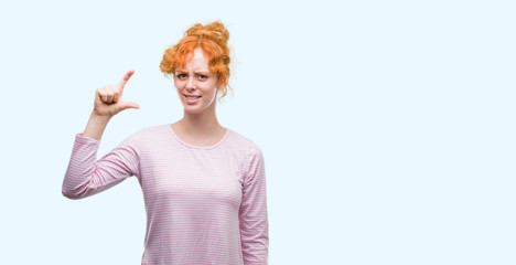 Wall Mural - Young redhead woman smiling and confident gesturing with hand doing size sign with fingers while looking and the camera. Measure concept.