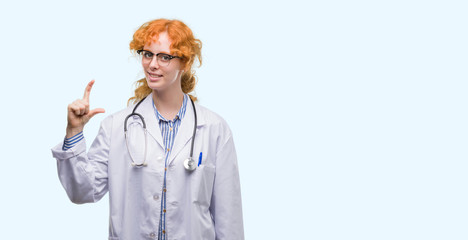 Poster - Young redhead woman wearing doctor uniform smiling and confident gesturing with hand doing size sign with fingers while looking and the camera. Measure concept.