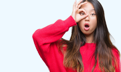 Young asian woman wearing winter sweater over isolated background doing ok gesture shocked with surprised face, eye looking through fingers. Unbelieving expression.