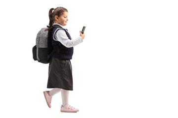 Wall Mural - Little schoolgirl in a uniform using a mobile phone and walking