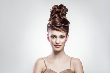 Wall Mural - portrait of attractive brunette woman with stylish hairdo and makeup looking at camera with smimle on isolated grey background. indoor, studio shot on copy space.