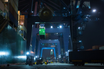 Wall Mural - Large mooring crane unloads container ship at night. Container terminal crane will load container onto vessel. Industrial Container yard for Logistic Import Export business