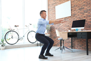 Young businessman doing exercises in office. Workplace fitness