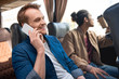 © LIGHTFIELD STUDIOS - smiling man talking on smartphone while his friend drinking coffee near during trip on travel bus