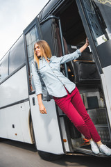 Wall Mural - low angle view of female tourist with backpack posing near travel bus at city street