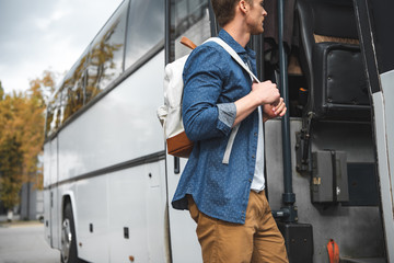 side view of male tourist with backpack walking into travel bus at urban street