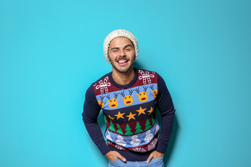 Wall Mural - Young man in Christmas sweater and knitted hat on color background