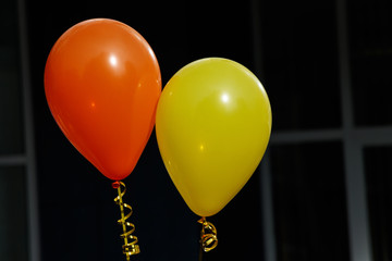 Orange and yellow balloon on dark background. The balls are tied with gold ribbons.