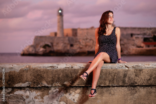 Photo Beautiful hispanic girl sitting on the Malecon seawall at sunset in Havana