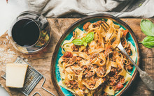 Italian Traditional Pasta Dinner. Flat-lay Of Tagliatelle Bolognese With Minced Meat, Tomato Sauce And Grated Parmesan Cheese And Glass Of Red Wine Over Rustic Wooden Board Background, Top View