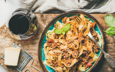 Wall Mural - Italian traditional pasta dinner. Flat-lay of Tagliatelle bolognese with minced meat, tomato sauce and grated parmesan cheese and glass of red wine over rustic wooden board background, top view