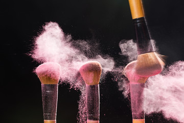 make up, beauty, mineral cosmetic concept - brush brushing away pink powder from another over the black background