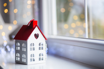 Toy house with hole in form of heart near window in daylight with garland lights on background.