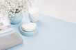 Cosmetics products background - set for body and skin care, blue ceramic bowl, silver accessories, flowers on white wood and color paper, blur, copy space.