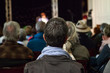 © Valmedia - Young man part of the audience is listening to a public conference given in a church - Pictured from the back with blurry people in the background