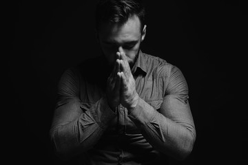 Wall Mural - Religious young man praying to God on dark background, black and white effect