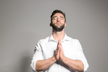 Wall Mural - Religious young man praying to God on light background