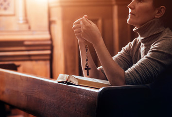 Wall Mural - Christian woman praying in church. Hands crossed and Holy Bible on wooden desk.