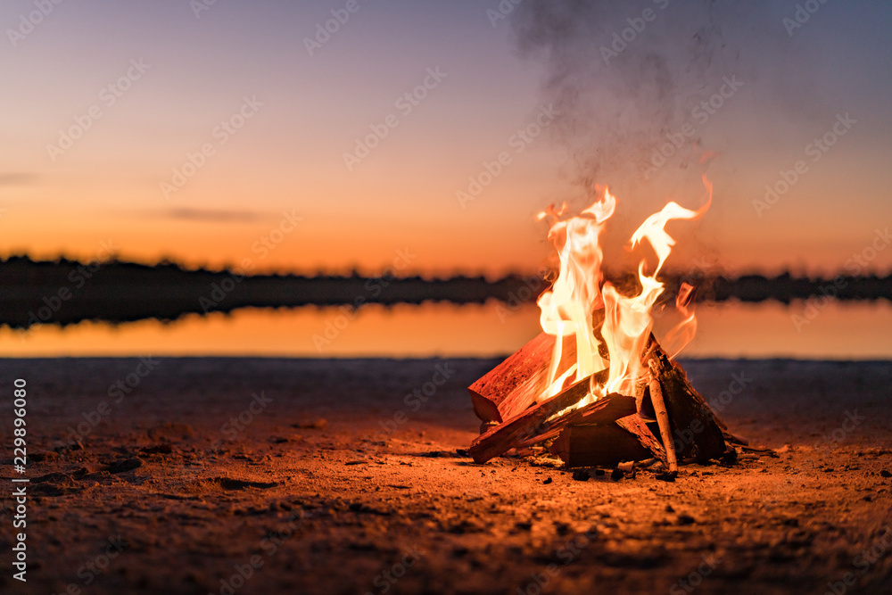 Small campfire with gentle flames beside a lake during a glowing sunset. Western Australia, Australia. - obrazy, fototapety, plakaty 