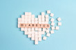 Broken heart made of sugar cubes with inscription diabetes on a blue background.