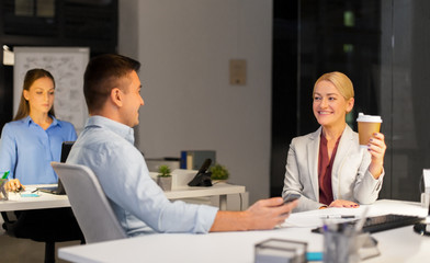 Poster - business, deadline and technology concept - businesswoman and businessman talking and drinking coffee late at night office