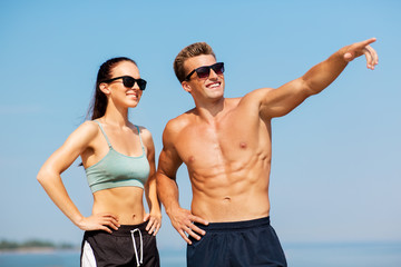 Poster - fitness, sport and lifestyle concept - happy couple in sports clothes and sunglasses on beach