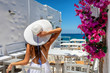 Frau in weißem Sommerkleid sitzt in einer Bar in dem idyllischem Fischerdorf Naousa auf Paros, Kykladen, Griechenland
