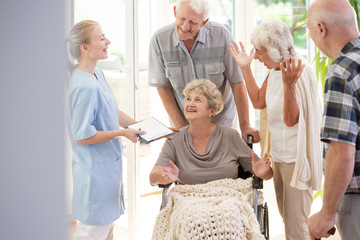 Poster - Smiling nurse talking with happy senior woman in the wheelchair and elderly people