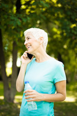 Wall Mural - Sporty senior woman using mobile phone in the park