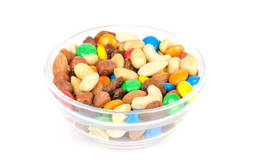 Wall Mural - Trail mix in glass bowl. Snack mix. Almonds, cashews, peanuts, hazelnuts, raisins and colorful chocolate candies. Food to be taken along hikes. Macro food photo closeup from above on white background.