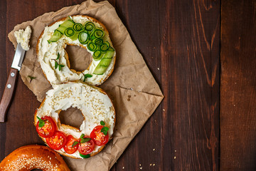 Bagels with cream cheese, sesame, tomato and cucumber on a wooden background. Top view flat lay. With copy space