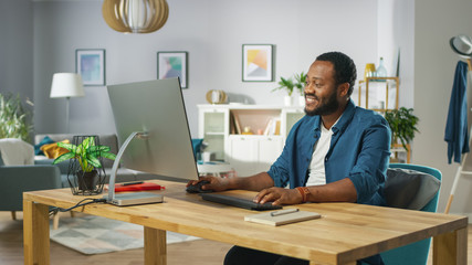 happy young man takes place at his desk and starts working on a personal computer. in the background
