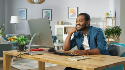 Wall Mural - Portrait of the Happy Man Sitting at His Desk, Watching Videos at Home. In the Background Cozy Living Room.