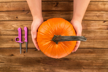 Wall Mural - Pumpkin in female hands on wooden table. Flat lay, top view fall autumn concept.