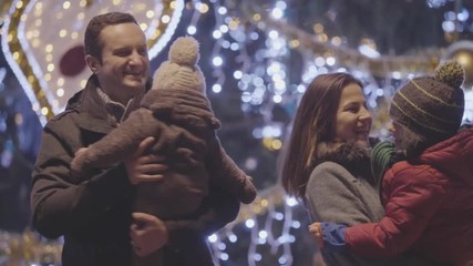 Wall Mural - Happy parents holding children dancing at Christmas tree, happy faces