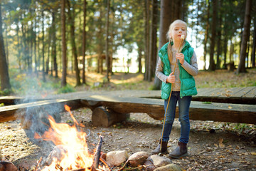 Wall Mural - cute little girl roasting marshmallows on stick at bonfire. child having fun at camp fire. camping w