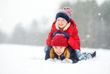 Fototapeta Nowy Jork - Two adorable little girls having fun together in beautiful winter park. Beautiful sisters playing in a snow.