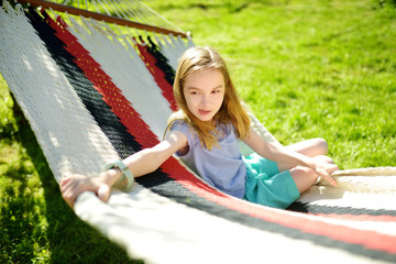 Happy little girl relaxing in hammock on beautiful summer day. Cute child having fun in spring garden.