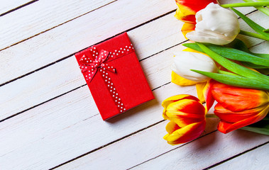 Beautiful bouquet of tulips and gift box on white wooden background