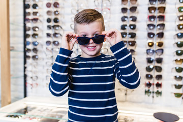 Wall Mural - Happy boy choosing sunglasses in optical store.