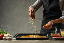 Chef Sprinkles Pizza With Cheese On The Background Of A Concrete Wall, With Free Space