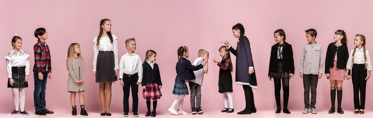 Cute smiling happy stylish children on pink background. Beautiful stylish teen girls and boy standing together and posing at studio. Classic style. Kids fashion and emotions concept.