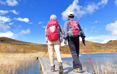 秋空と紅葉の草原を歩く二人 