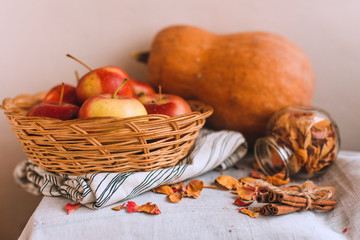 Still life with cinnamon sticks wrapped in twine, apples in a wicker basket stand on a striped linen cloth, walnuts and flower petals. Concept of home comfort in autumn or winter.