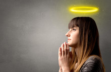 Young Woman Praying On A Grey Background With A Shiny Yellow Halo Above Her Head
