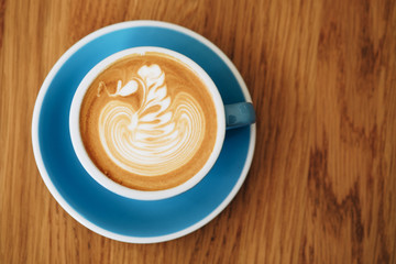 A cup of latte art coffee blue color mug ceramic swan shape beautiful foam on wooden table desk background.