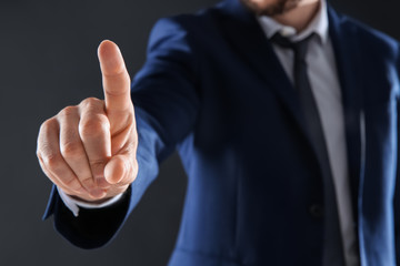 Businessman touching empty virtual screen against dark background, focus on hand