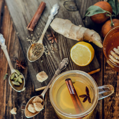 Vitamin healing tea with lemon and honey, ginger and spices on wooden background in rustic style. The concept of spring beriberi and colds. Square image.