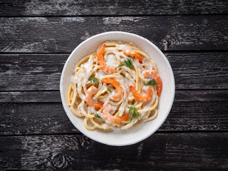 Wall Mural - italian pasta spaghetti with shrimps, bechamel sauce and chopped dill on dark rustic wooden table, top view